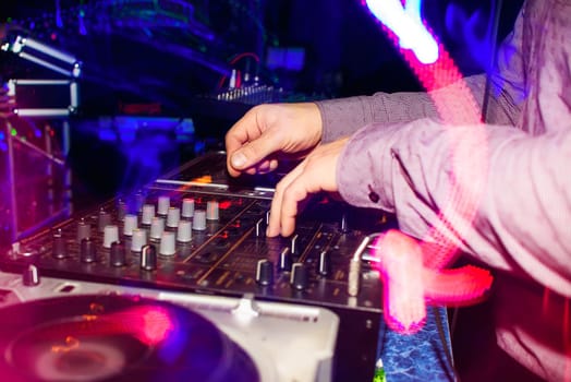 DJ hands mix music on professional mixer in booth at a party in nightclub