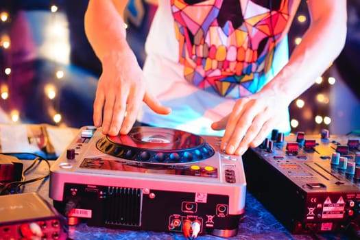 DJ in the night club brings music to the console in bright colored colors
