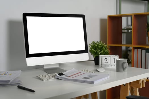Blank screen computer desktop on white table with financial reports and coffee cup.