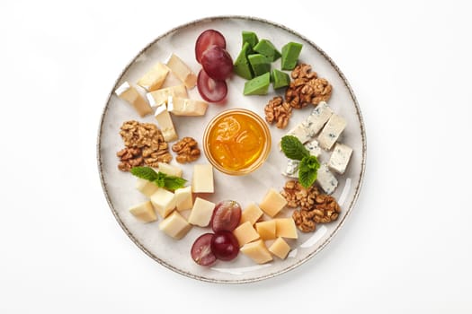 Delicious platter with slices of soft and firm cheeses, dor blue and green pesto cheese. Five varieties of cheese traditionally served with honey, grape and walnuts on plate garnished with fresh mint