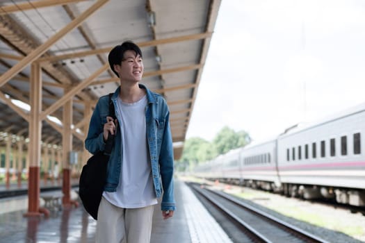 A young man carries a backpack and waits for the train at the train station to travel..