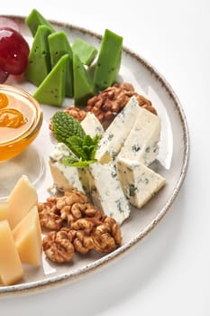 Closeup of vintage ceramic plate with dor blue, green pesto cheese and parmesan served with clear honey, purple grapes and walnuts garnished with fresh mint. Traditional cheese platter