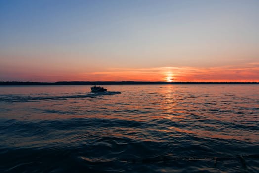 boat floats on the water waves on the background of red and blue sunset with the sun