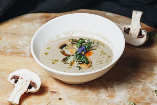 A bowl of soup filled with mushrooms and herbs sitting on a wooden cutting board.