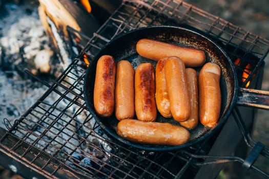 sausages fried in a pan on the grate of the fire on the camping