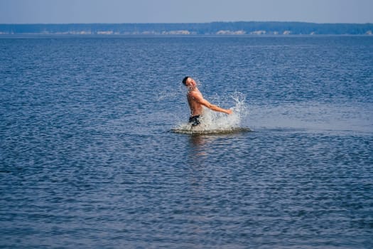 young man swims and having fun resting in the water with the spray in summer on the beach