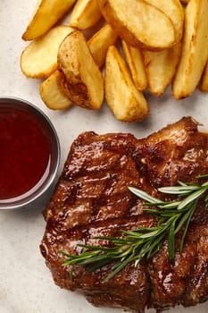 Closeup of appetizing juicy fried pork steak with side dish of crispy potato wedges and barbecue sauce on speckled ceramic plate garnished with fresh aromatic rosemary