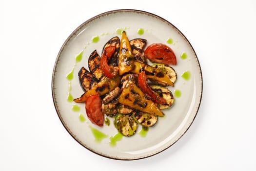 Grilled slices of zucchini, eggplant, bell pepper, tomato and mushrooms drizzled with vibrant green herb sauce served on speckled plate, top view. Vegetarian dish for healthy and delicious snacking