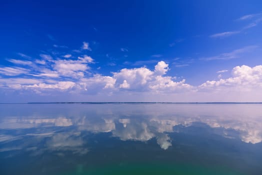blue clear sky with white clouds reflected in the calm water of the sea on a Sunny day