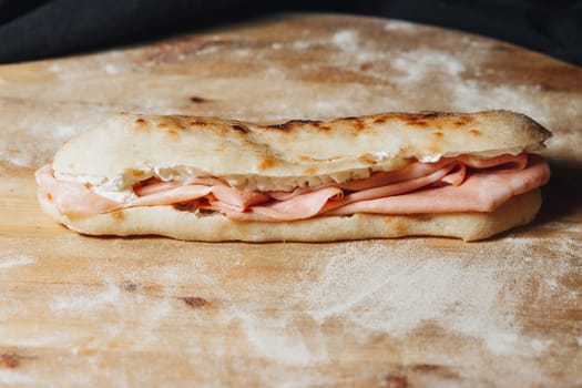 A delectable sandwich with ham and cheese ingredients, placed on a wooden cutting board.