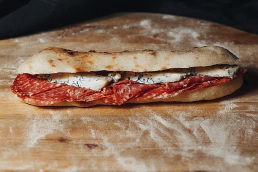 A delicious sandwich featuring layers of savory meat and rich cheese resting on a rustic wooden cutting board.