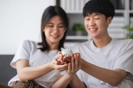 Young couple sitting together on the sofa Holding a pig model, concept of saving money.