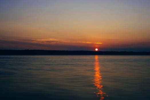 sunset over the river with the sun and the silhouette of the shore on a warm summer evening