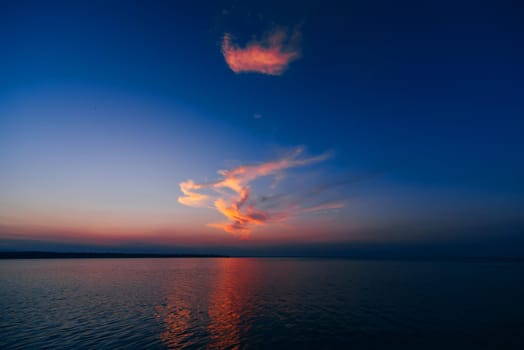 sunset over sea with blue sky and red clouds reflected in water