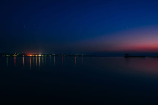 city on the banks of the river and jetty at dawn at night with blue sky and stars