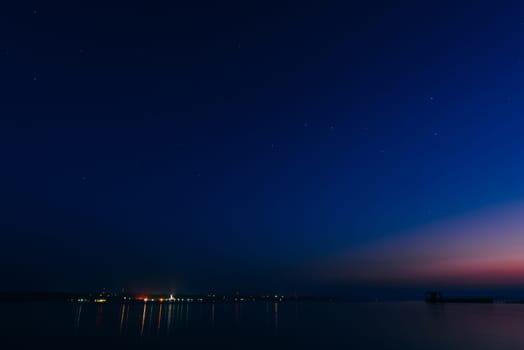 starry night sky with stars and the glowing city on the banks of the river