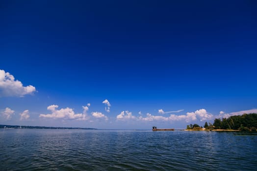 blue sky over the water of the river with a jetty and a sandy beach on a summer day