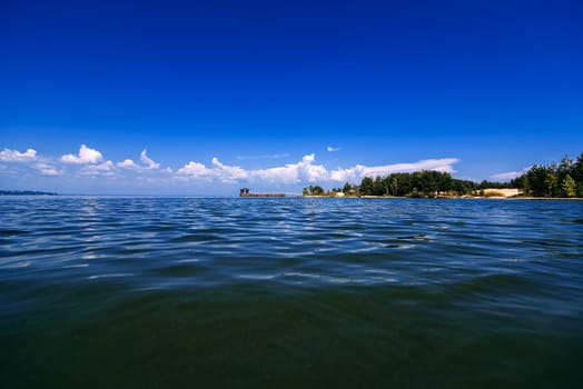 blue sky with white clouds over the water on a summer day with a jetty and shore in the distance