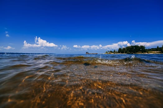blue clear sky with white clouds over the water on a summer day and a beach with waves
