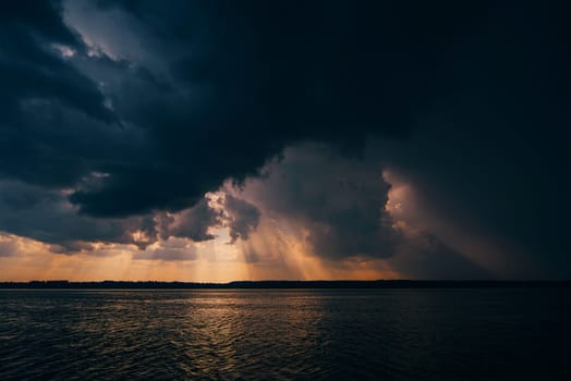 dramatic dark sky with rain clouds and sun over the river in the evening summer sunset