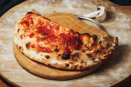 A golden-brown calzone filled with melted cheese and rich tomato sauce atop a circular wooden board.