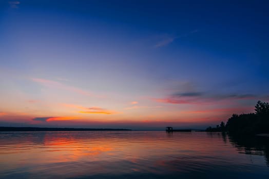 sunset over the water of the river with a pier and a beach with a beautiful red and blue sky