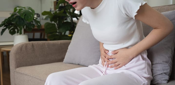 A young Asian woman with abdominal pain from diarrhea or menstrual cramps felt sick and touched her stomach with an unhappy expression..