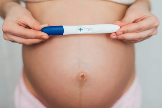 a positive pregnancy test in the hands of a pregnant young girl on the background of belly