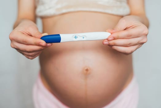 positive pregnancy test in the hands of a pregnant girl on the background of the abdomen