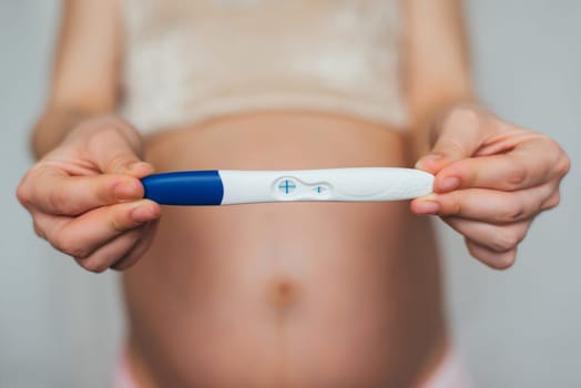 positive pregnancy test in the hands of a pregnant girl on the background of the abdomen