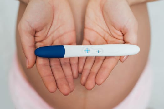 positive pregnancy test in the hands of a pregnant girl on the background of the abdomen
