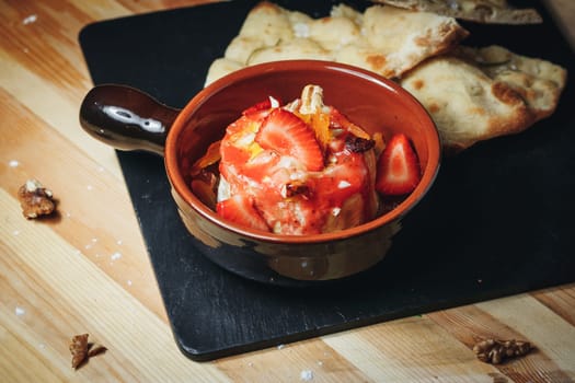 A bowl of ripe red strawberries and slices of bread placed together on a wooden table, creating a vibrant and inviting setting.