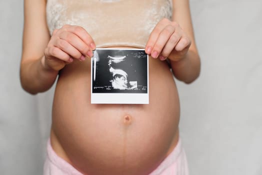 ultrasound picture in the hands of a pregnant girl on the background of the abdomen
