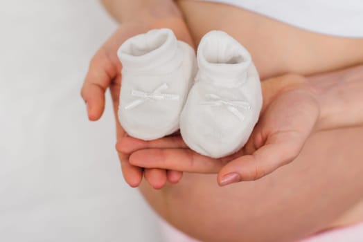 hands of a pregnant woman with booties for a newborn on the background of belly