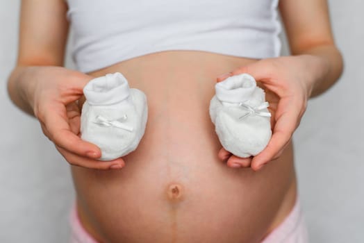 booties for newborn in the hands of a pregnant girl on the background of the abdomen waiting for the baby