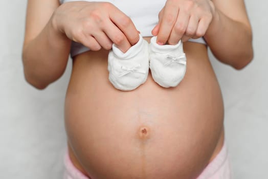 booties for newborn in the hands of a pregnant girl on the background of the abdomen