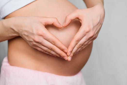 pregnant girl makes a hands love heart on the background of belly