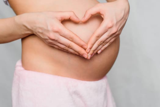 pregnant girl makes a hands love heart on the background of belly