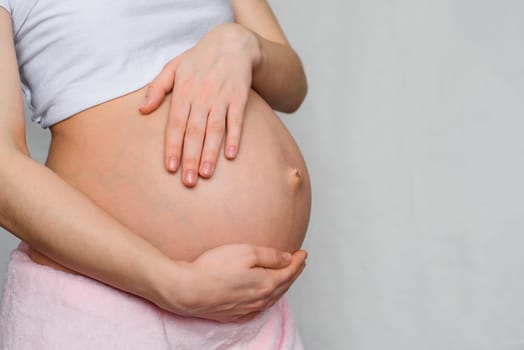 pregnant girl hugging her belly with her hands closeup