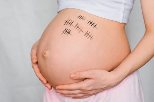 pregnant girl hugs her stomach with a term of pregnancy drawn on it
