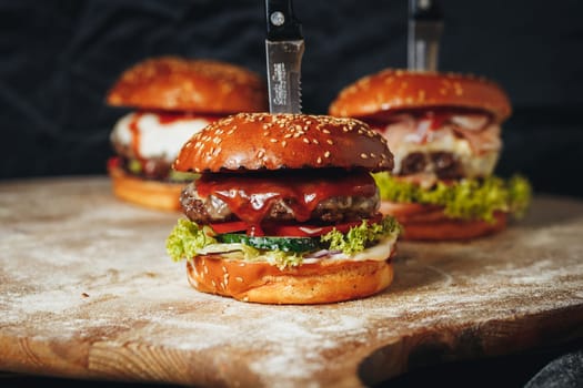 Three juicy burgers beautifully displayed on a wooden cutting board with a sharp knife ready for slicing.