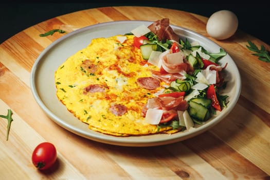 A colorful omelet with a medley of vegetables and savory meats served on a white plate.