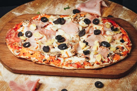 A delicious pizza topped with succulent ham slices and flavorful olives rests on a rustic wooden cutting board.