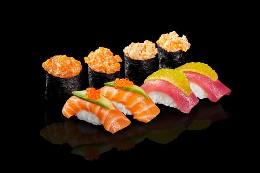 Vibrant set of gunkan maki with creamy seafood topping and nigiri sushi with fresh salmon and tuna garnished with cucumber, caviar and orange pulp on black reflective surface. Japanese style snacks