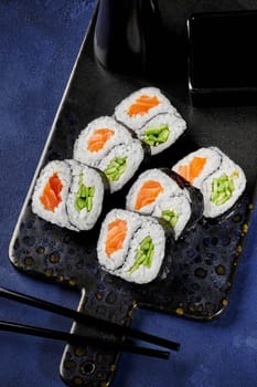 Delicious salmon and cucumber futomaki rolls with yin-yang design traditionally served with soy sauce on serving board against blue textured surface. Creative take on Japanese sushi presentation
