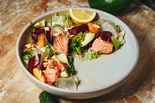 A vibrant bowl of succulent salmon and colorful assorted vegetables arranged elegantly on a rustic wooden table.