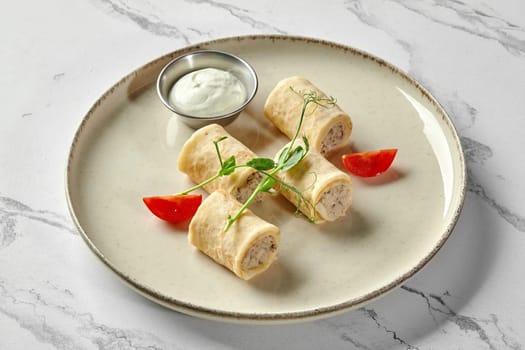 Delicious savory thin crepes filled with ground chicken meat garnished with cherry tomato slices and microgreens, served with sour cream on plate against marble backdrop