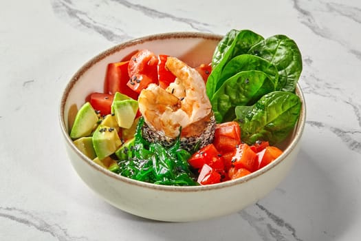 Appetizing salad of fried shrimps with sprouted seeds, fresh vegetables, greens, avocado and chuka seaweed served in ceramic bowl on marble background
