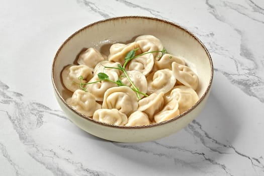 Rustic bowl filled with freshly boiled dumplings, garnished with sprig of green, presented on marbled surface. Traditional Eastern European comfort food