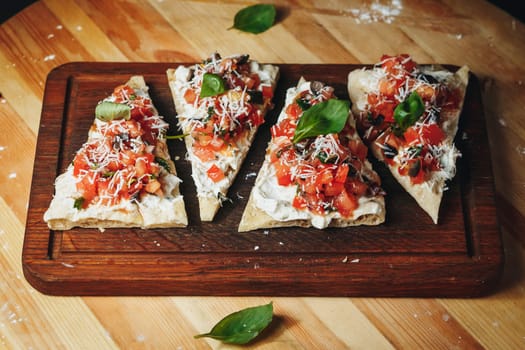 Four delicious slices of pizza garnished with fresh tomatoes and basil arranged on a rustic wooden cutting board.